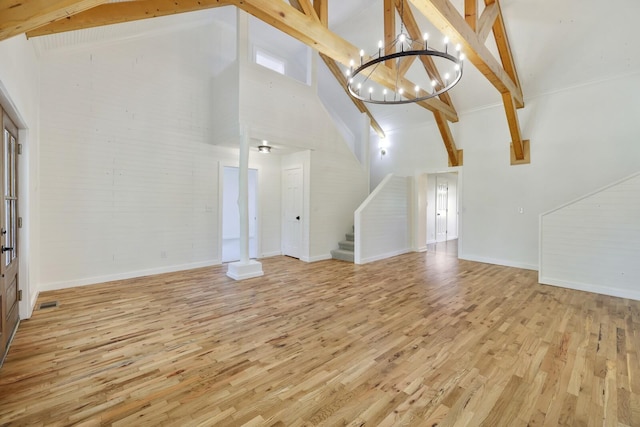 unfurnished living room with high vaulted ceiling, light wood-type flooring, stairs, a chandelier, and beamed ceiling