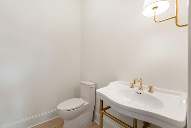 bathroom with baseboards, toilet, wood finished floors, and a sink