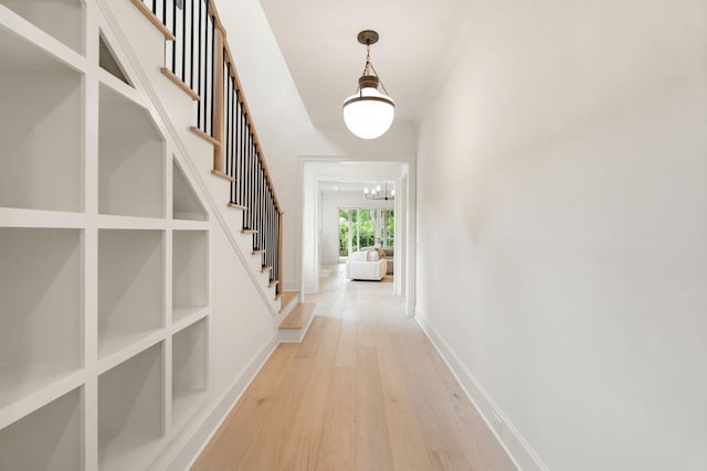 hall featuring a chandelier, light wood-style floors, stairway, and baseboards