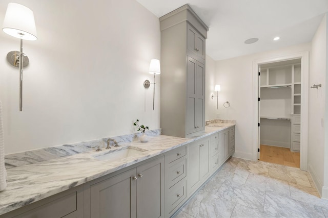 bathroom with vanity, a walk in closet, baseboards, and marble look tile flooring