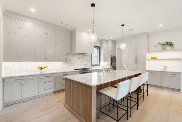 kitchen with open shelves, light wood finished floors, decorative backsplash, appliances with stainless steel finishes, and a kitchen bar