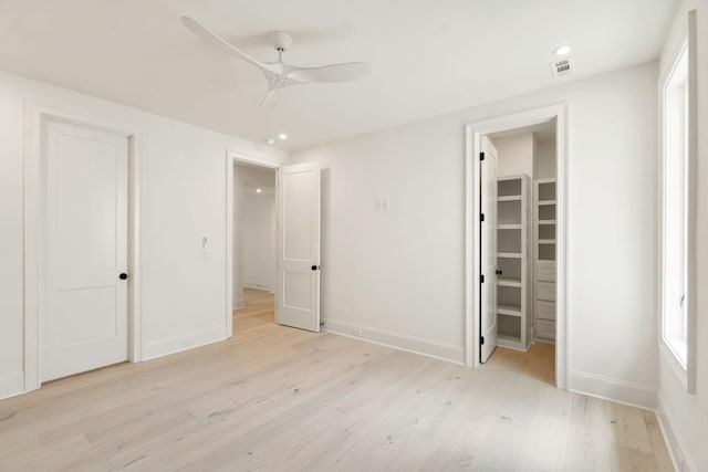 unfurnished bedroom featuring a closet, light wood-style floors, baseboards, recessed lighting, and a walk in closet