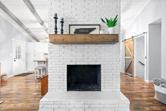 detailed view of a barn door, a brick fireplace, wood finished floors, baseboards, and beam ceiling