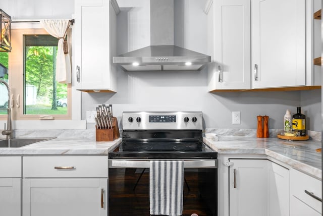 kitchen featuring stainless steel electric range oven, wall chimney exhaust hood, white cabinetry, and a sink
