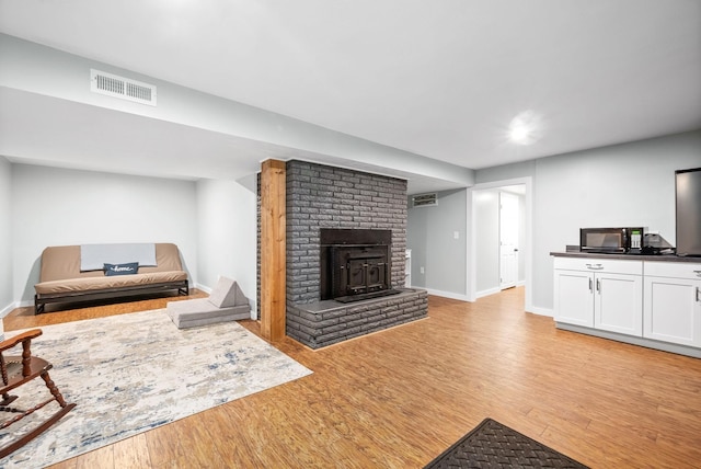 living area featuring light wood-style floors, baseboards, and a brick fireplace