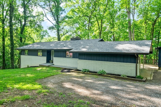 view of front of property with a chimney, brick siding, a shingled roof, and a front lawn