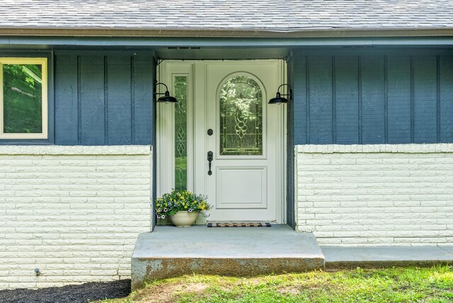 doorway to property with board and batten siding, a shingled roof, and brick siding