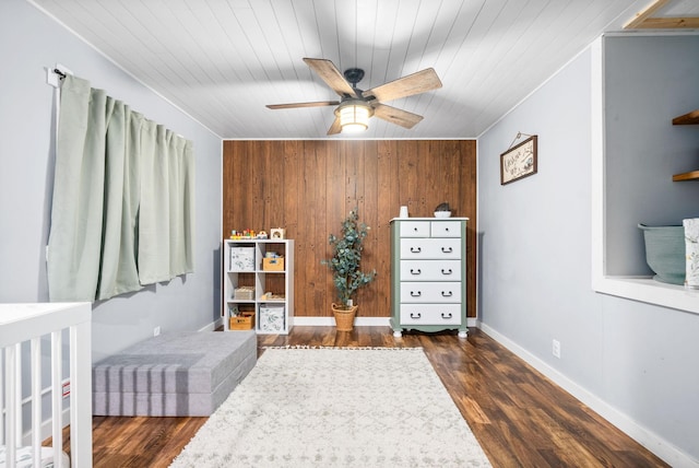 bedroom featuring wooden ceiling, dark wood-type flooring, wooden walls, baseboards, and a ceiling fan