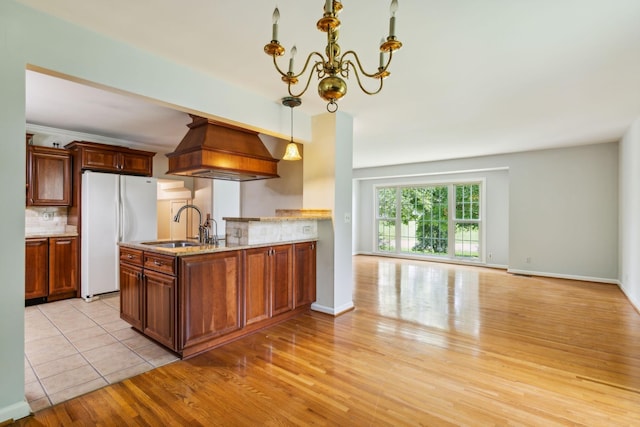 kitchen with freestanding refrigerator, a sink, a chandelier, light stone counters, and light wood-style flooring