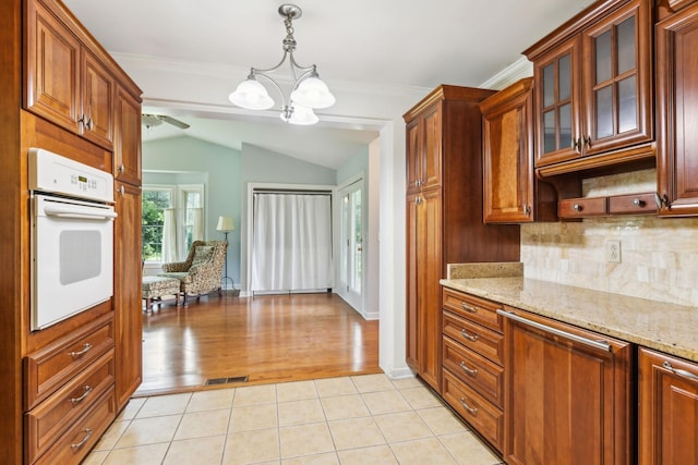 kitchen featuring oven, vaulted ceiling, backsplash, a chandelier, and light stone counters