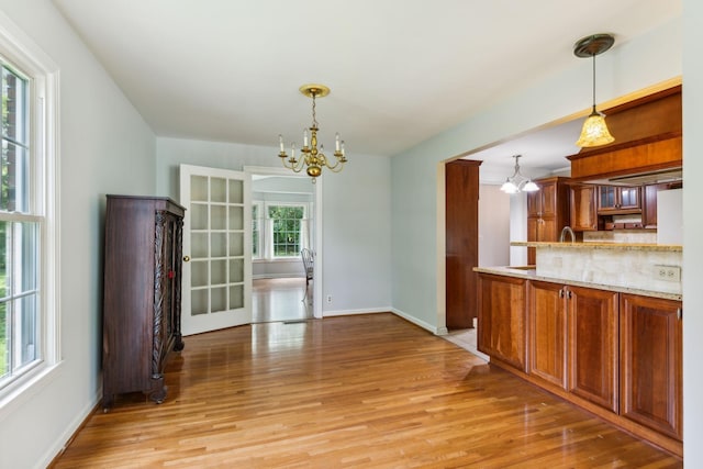 unfurnished dining area featuring a chandelier, light wood finished floors, and baseboards