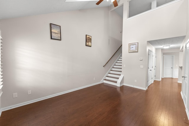 unfurnished living room with ceiling fan, stairs, hardwood / wood-style floors, baseboards, and high vaulted ceiling