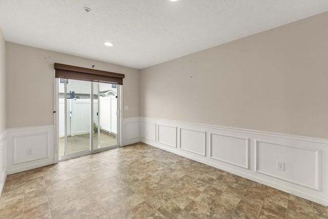 empty room with wainscoting, recessed lighting, a decorative wall, and stone finish flooring