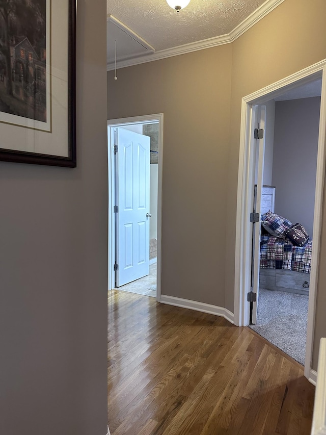 hall featuring attic access, ornamental molding, wood finished floors, a textured ceiling, and baseboards