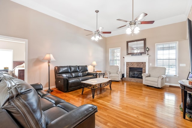 living area with light wood-style floors, a ceiling fan, a fireplace, baseboards, and crown molding