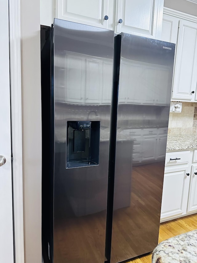 kitchen view of white cabinetry, light wood finished floors, light stone counters, tasteful backsplash, and stainless steel fridge with ice dispenser