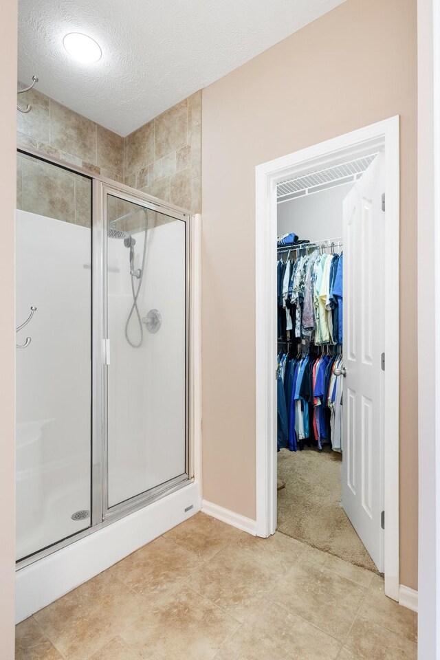 bathroom with a shower stall, a textured ceiling, baseboards, and a walk in closet