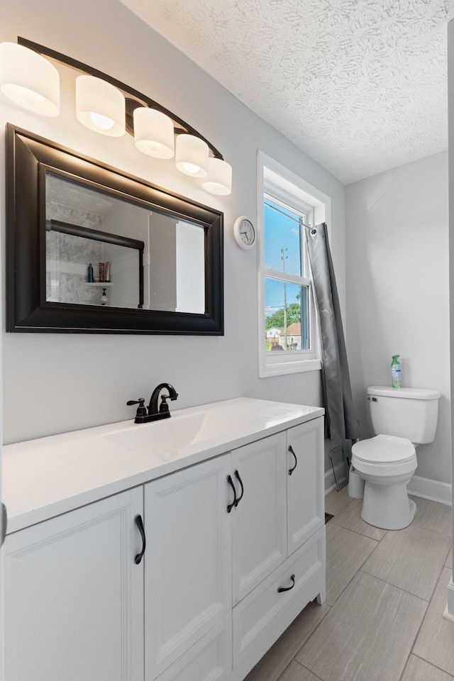 bathroom with vanity, toilet, a textured ceiling, and baseboards