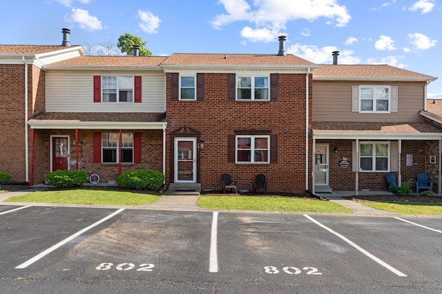 townhome / multi-family property with uncovered parking, brick siding, and roof with shingles
