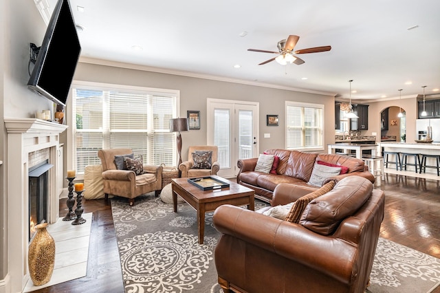 living area featuring a ceiling fan, healthy amount of natural light, a high end fireplace, ornamental molding, and arched walkways