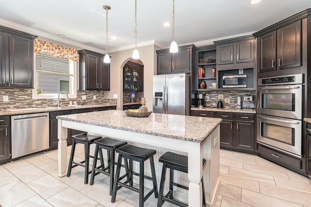 kitchen featuring stainless steel appliances, arched walkways, decorative backsplash, a center island, and a sink