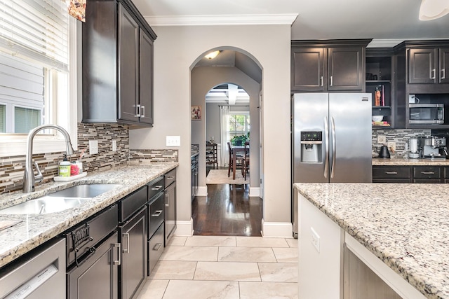 kitchen featuring a sink, appliances with stainless steel finishes, tasteful backsplash, light stone counters, and ornamental molding