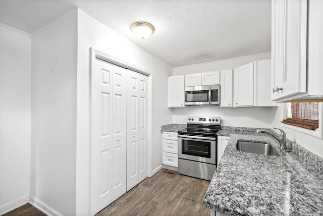 kitchen featuring stainless steel appliances, a sink, dark wood finished floors, white cabinetry, and a textured ceiling