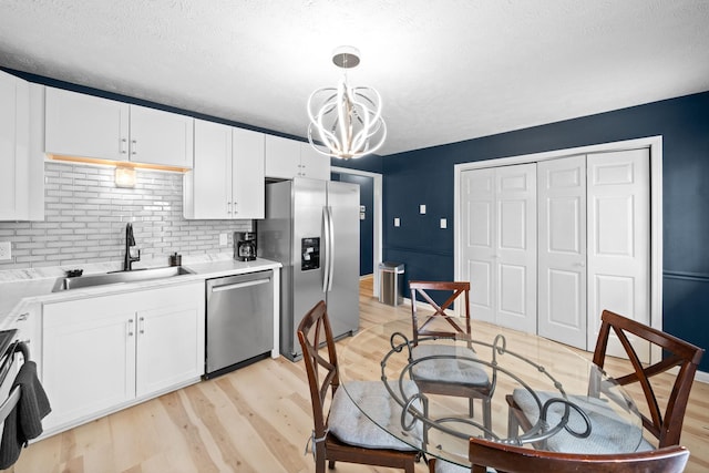 kitchen with appliances with stainless steel finishes, a sink, a chandelier, light wood-style flooring, and white cabinetry