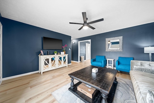 living area with ceiling fan, an accent wall, wood finished floors, and baseboards