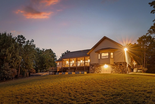 back of property at dusk with stone siding and a lawn