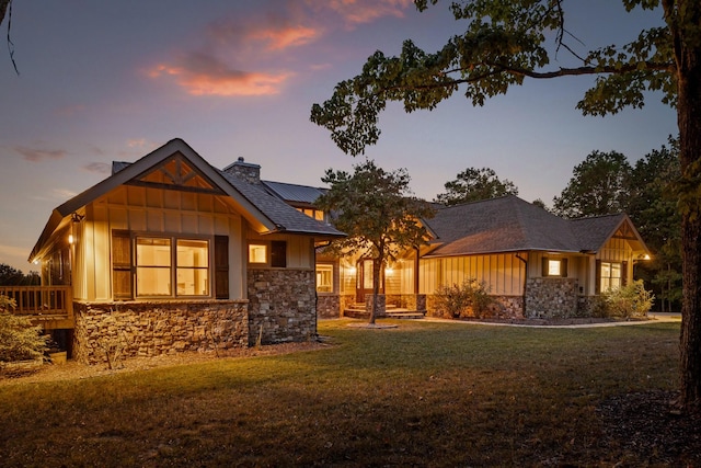 view of front facade featuring board and batten siding, stone siding, a chimney, and a yard