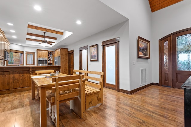 dining area with hardwood / wood-style flooring, baseboards, ceiling fan, a raised ceiling, and arched walkways