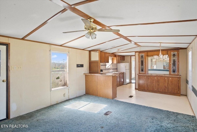 kitchen with brown cabinets, a peninsula, a chandelier, light carpet, and freestanding refrigerator
