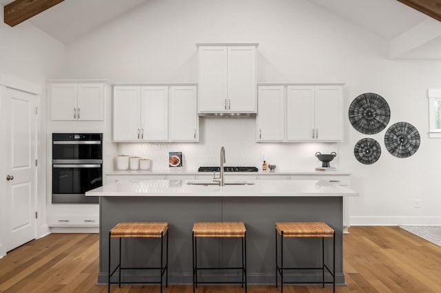 kitchen with double wall oven, light countertops, backsplash, a kitchen breakfast bar, and high vaulted ceiling