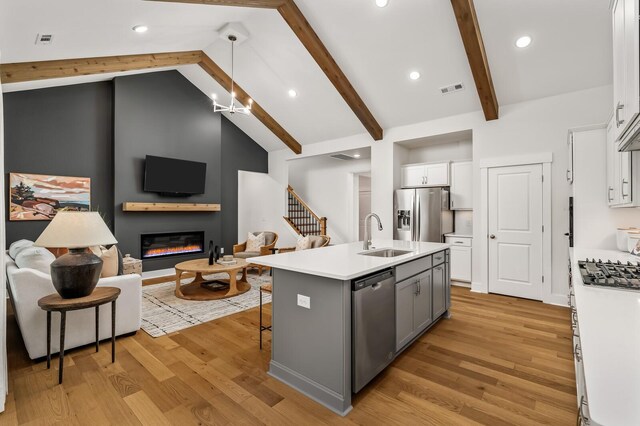 kitchen featuring stainless steel appliances, a sink, a glass covered fireplace, open floor plan, and white cabinetry