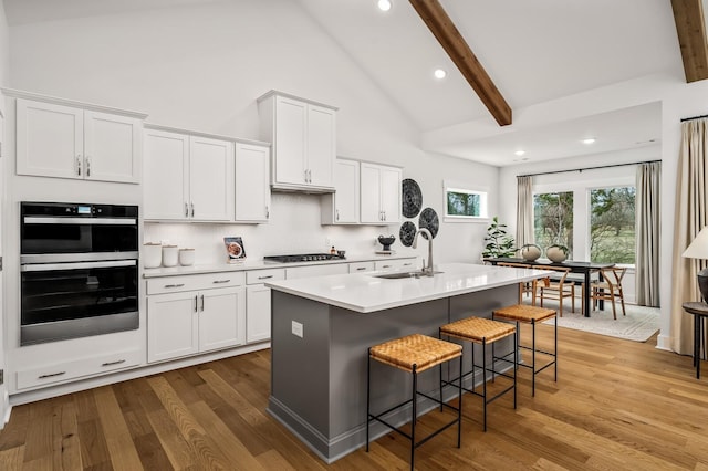 kitchen featuring a sink, gas cooktop, wood finished floors, beam ceiling, and a kitchen bar