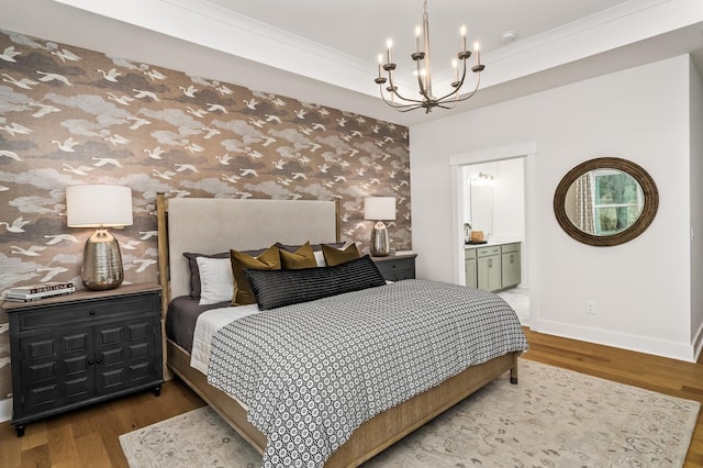 bedroom featuring a chandelier, baseboards, wood finished floors, crown molding, and ensuite bath