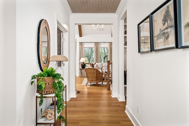hallway featuring wood finished floors, a chandelier, baseboards, and ornamental molding