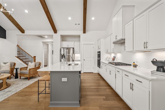kitchen with stainless steel appliances, a sink, light wood-style floors, white cabinets, and tasteful backsplash