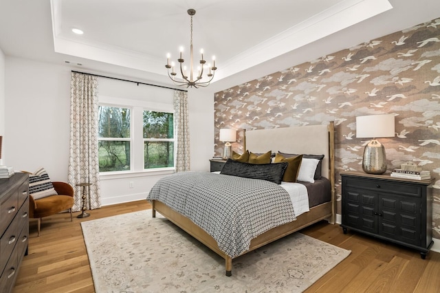 bedroom featuring a chandelier, light wood-style flooring, a tray ceiling, wallpapered walls, and baseboards