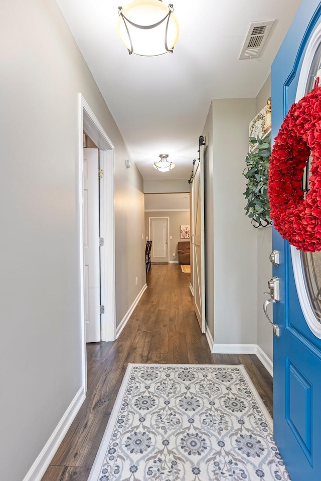 corridor with a barn door, dark wood-style flooring, and baseboards