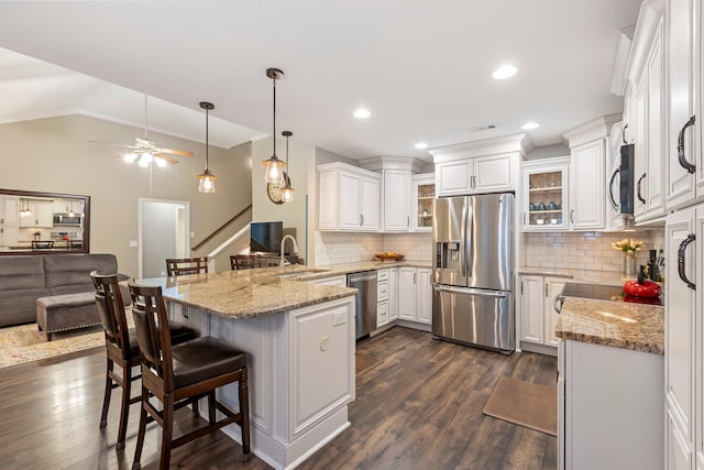 kitchen featuring stainless steel appliances, a peninsula, open floor plan, a sink, and white cabinetry