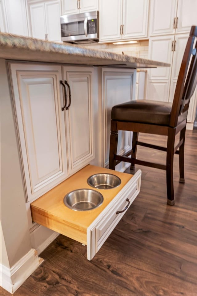kitchen view of stainless steel microwave, dark wood-style floors, baseboards, and white cabinets