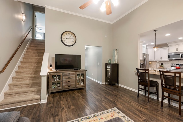 living area with ceiling fan, stairs, dark wood finished floors, baseboards, and crown molding