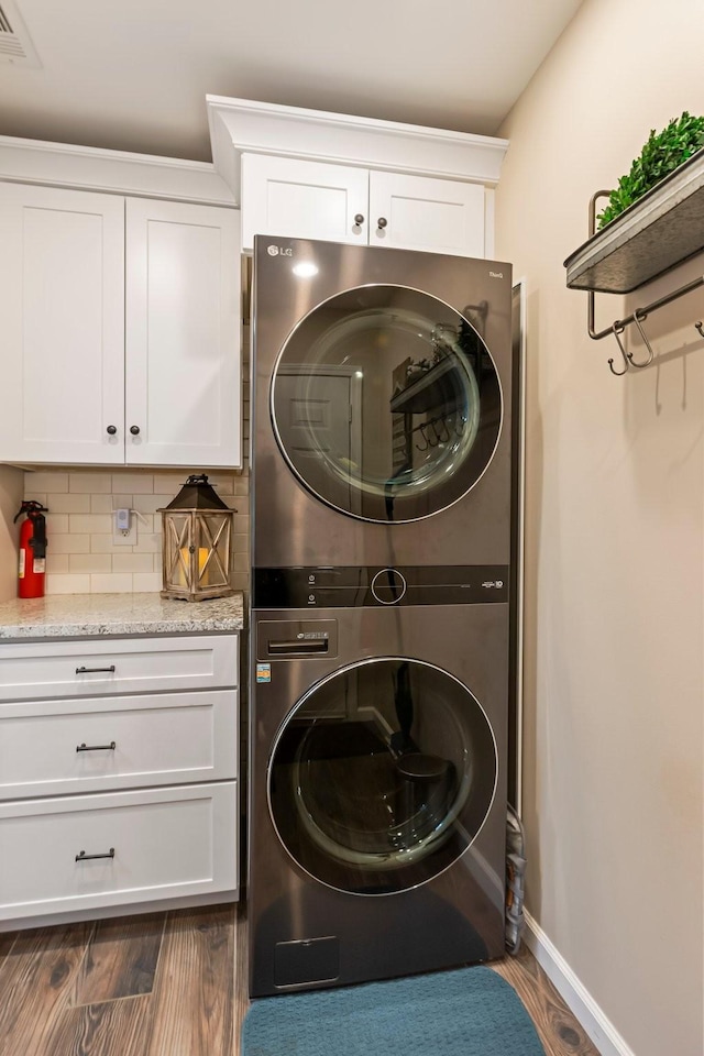 laundry area featuring estacked washer and dryer, dark wood-style flooring, baseboards, and cabinet space
