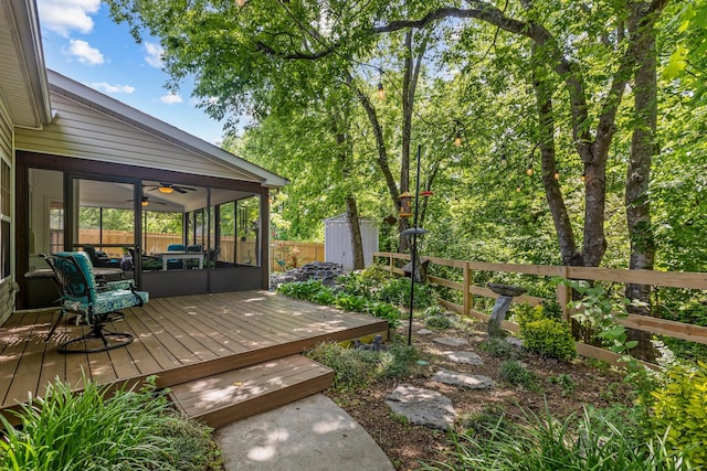 deck with a storage unit, a sunroom, an outbuilding, fence, and ceiling fan