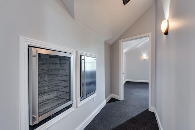 hallway with dark colored carpet, vaulted ceiling, and baseboards