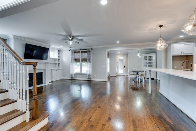 unfurnished living room with ceiling fan, stairs, crown molding, a premium fireplace, and dark wood finished floors