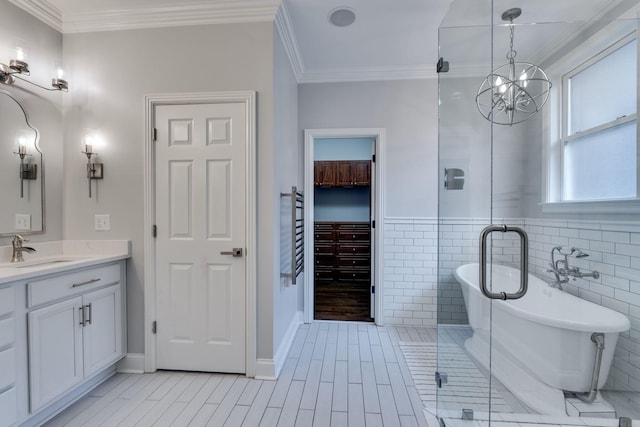 bathroom with ornamental molding, a freestanding bath, vanity, a chandelier, and tile walls