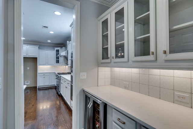 bar area featuring beverage cooler, ornamental molding, dark wood-type flooring, stainless steel range, and backsplash